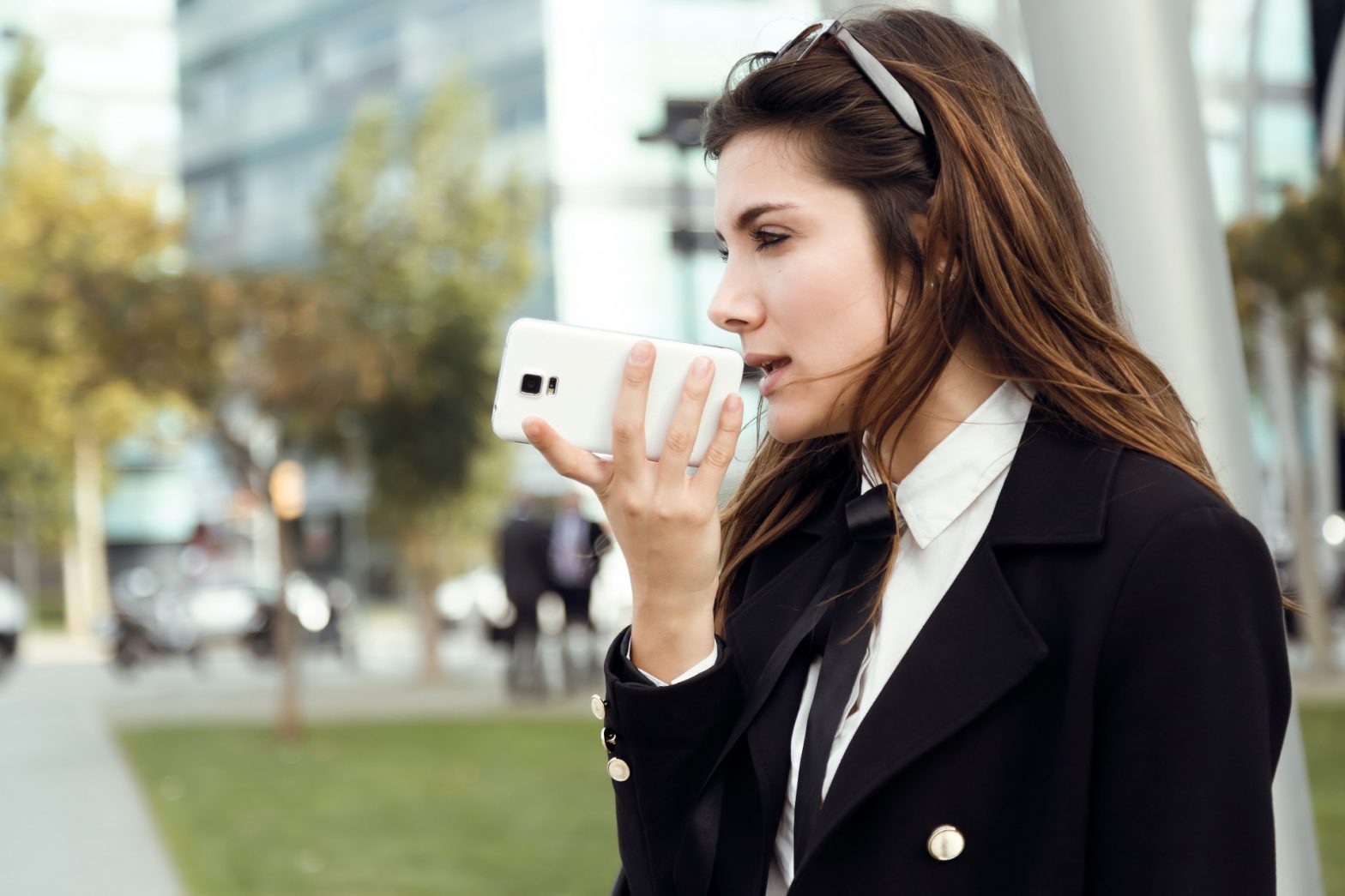 Mujer de negocios utilizando una aplicación de voz a texto en su teléfono mientras está al aire libre.