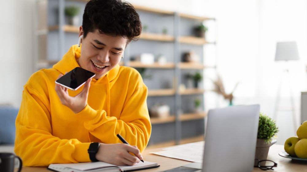asiatischer mann mit gelbem pullover benutzt gerät, um stimme in text zu übersetzen