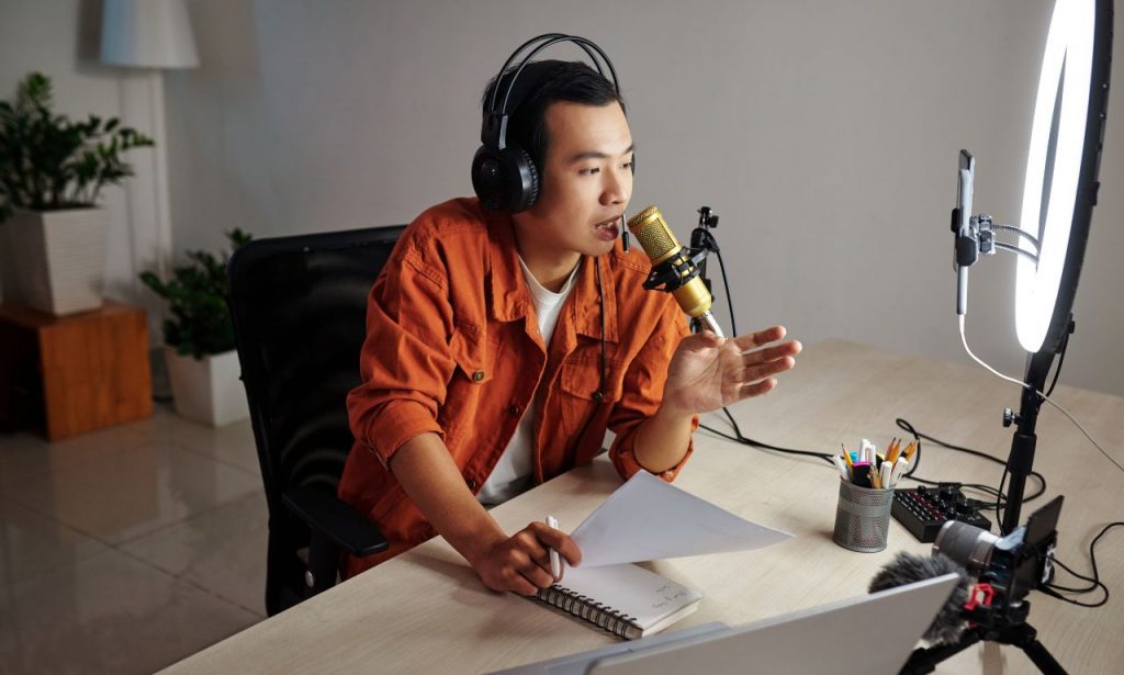 Asian descent man speaking to his podcast audience while transcribing notes