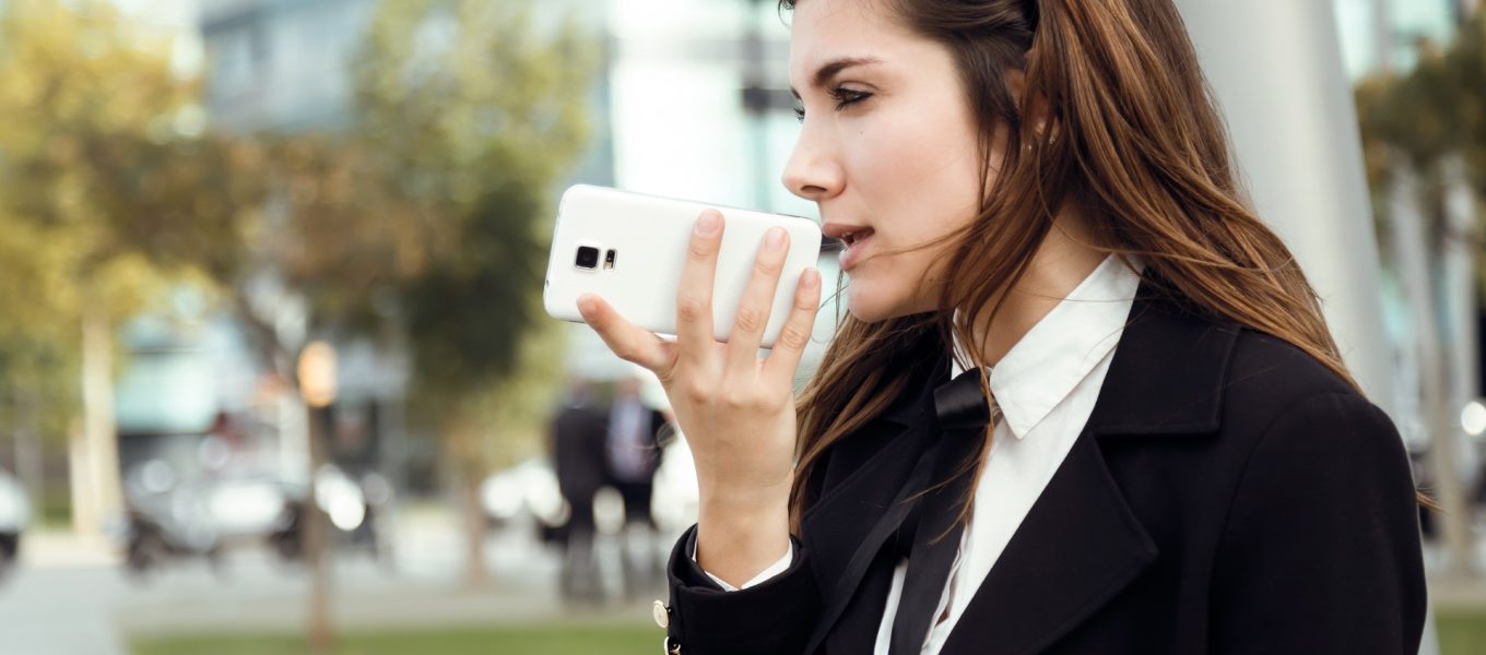 Geschäftsfrau, die auf ihrem Telefon eine App zur Umwandlung von Sprache in Text verwendet, während sie sich im Freien aufhält